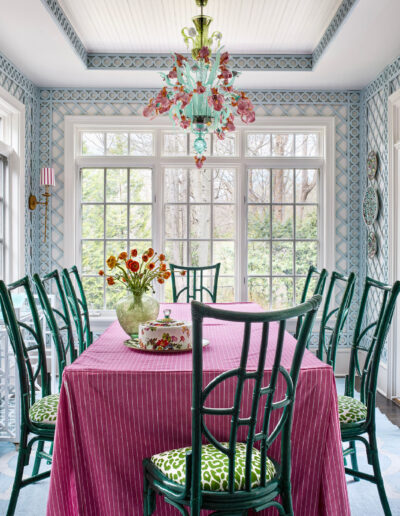 A dining room table with green chairs and pink tablecloth.