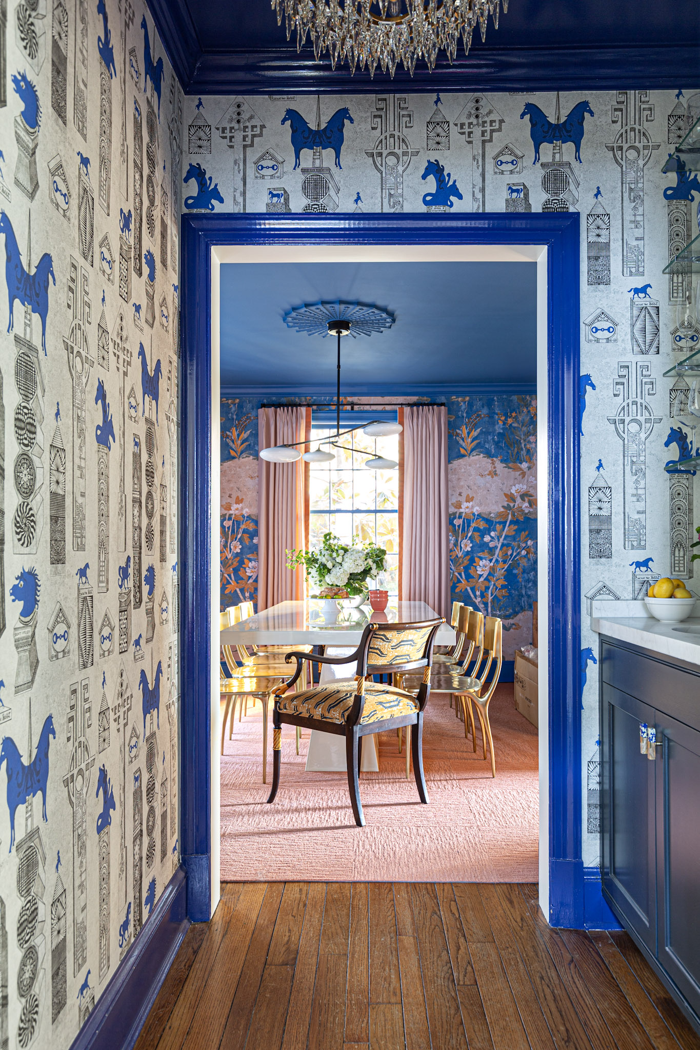 blue, white, and pink dining room, chinoiserie wallpaper, visual comfort lighting, with custom chrome bar rods and a marble counter top. blue and white Jennifer Shorto horse wallpaper adorns the walls of a wet bar leading into a blue and pink dining room, Luxury design, colorful design, famous designer, washington dc, virginia, maryland