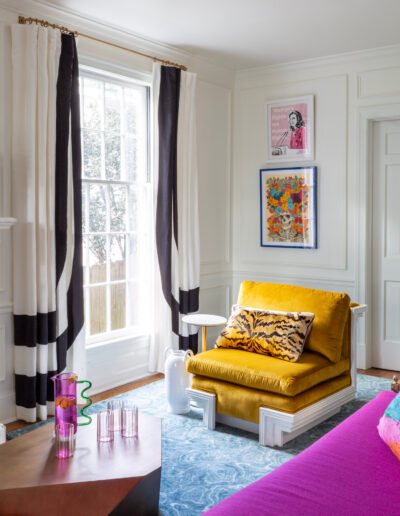 A living room with black and white curtains, yellow chair and pink table.