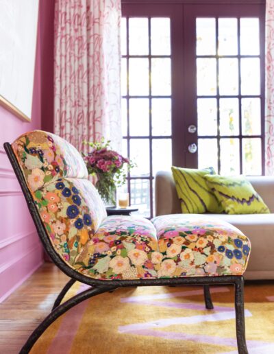 A colorful chair in front of a window with pink curtains.